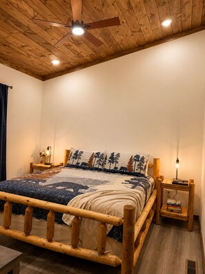 A bedroom with a wooden bed frame, a ceiling fan, bedside lamps, and a nightstand with books. - Beautiful Views in Gatlinburg's Art District (Gatlinburg)