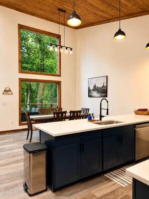 A modern kitchen with a large island, wooden ceiling, and large windows overlooking greenery. - Beautiful Views in Gatlinburg's Art District (Gatlinburg)