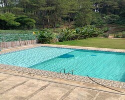 Una piscina rectangular con borde de azulejos, rodeada por un deck de concreto y una valla de madera.