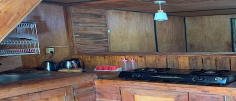 Cocina rústica con armarios de madera, estufa a gas y una lámpara colgante.