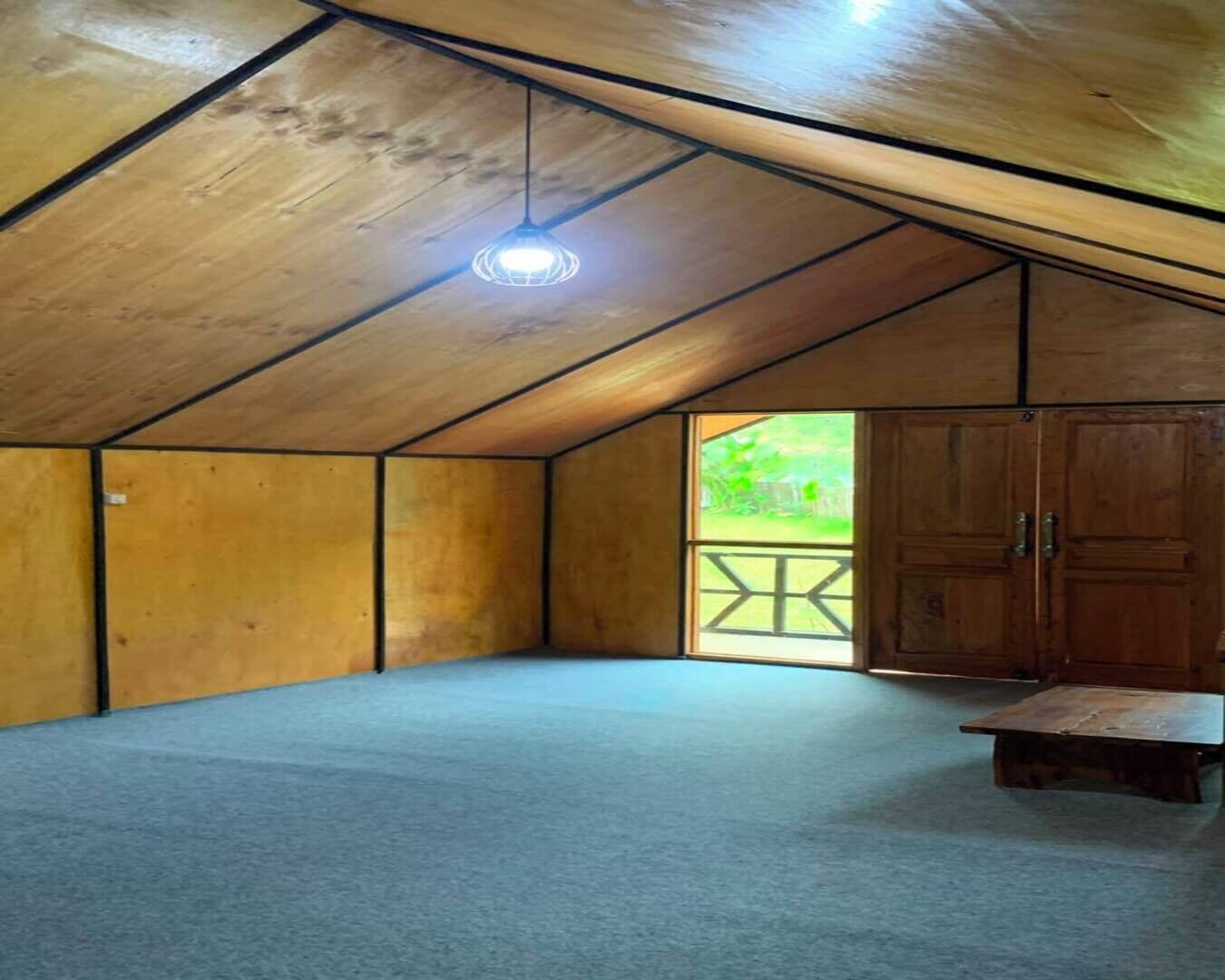 Una habitación con techo inclinado, una lámpara sencilla, vista por una puerta y una mesita pequeña.