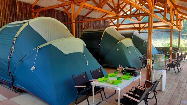 A covered outdoor area with multiple tents and a table with chairs and camping gear. - Cozzy Taman Nyingkur (bandung)