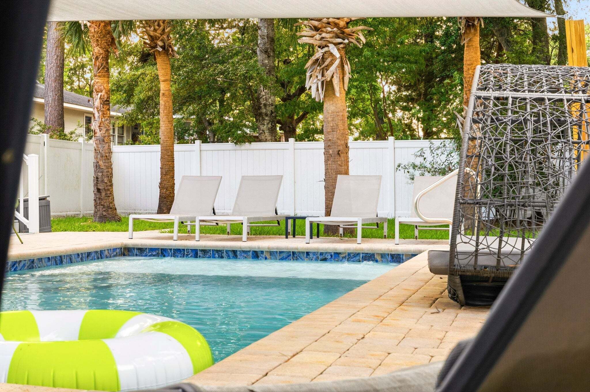 Una piscina con sillas de descanso y una valla blanca al fondo.