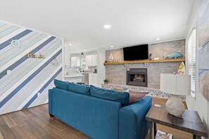 Ein modernes Wohnzimmer mit einem blauen Sofa, einem Kamin und einer Küche im Hintergrund.