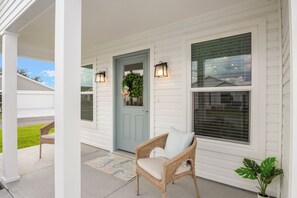 A porch with a wicker chair and a door with a wreath.