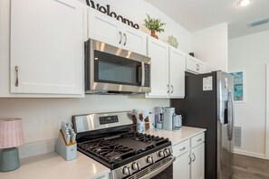 A modern kitchen with white cabinetry, a stainless steel microwave, a gas stove, and a black refrigerator.
