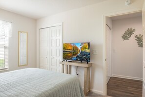 A bedroom with a bed, a television on a stand, a door, and a window with blinds.