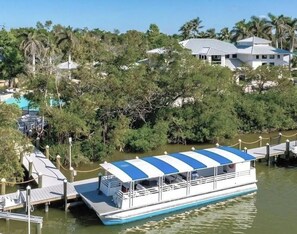 A riverboat docked at a pier with a covered deck, surrounded by trees and a residential area in the background. - Luxury3BRNaplesCondo-Optional Club Membership- Beach Shuttle to Wiggins pass (Naples)