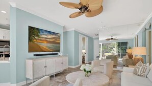 A spacious living room with a large flat-screen TV, a ceiling fan, and a dining area with natural light. - Luxury3BRNaplesCondo-Optional Club Membership- Beach Shuttle to Wiggins pass (Naples)