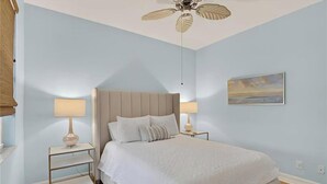 A bedroom with a bed, two bedside tables with lamps, a ceiling fan, and a painting on the wall. - Luxury3BRNaplesCondo-Optional Club Membership- Beach Shuttle to Wiggins pass (Naples)