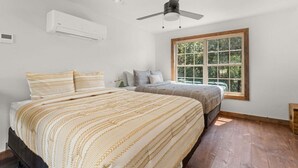 Un dormitorio con dos camas, ventilador de techo, aire acondicionado y un amplio ventanal con vistas a zonas verdes.