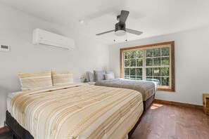 A bedroom with two beds, a ceiling fan, an air conditioning unit, and a large window with a view of greenery. - Cozy Cabin_Peaceful Wooded Views_Free Attraction Tickets_Deck Space (Branson)
