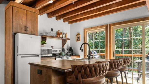 Una cocina con una isla central, taburetes de bar, vigas de madera y un ventanal grande.