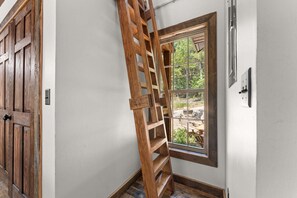 A wooden ladder leaning against a white wall next to a window with a view of an outdoor area. - Cozy Cabin_Peaceful Wooded Views_Free Attraction Tickets_Deck Space (Branson)