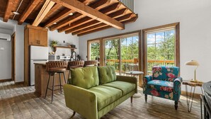 A spacious living area with a high ceiling, a kitchen, and large windows offering a view of the outdoors. - Cozy Cabin Tucked Away w Free Attraction Tickets_Deck Space_Bonus Loft_Near Branson (Branson)