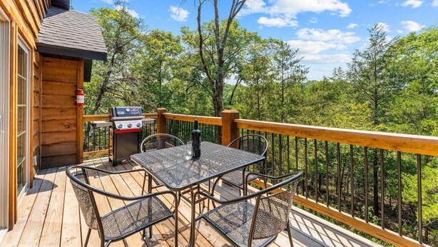A wooden deck with a grill, table, and chairs, overlooking a forested area. - Cozy Cabin Tucked Away w Free Attraction Tickets_Deck Space_Bonus Loft_Near Branson (Branson)