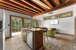 A spacious kitchen with a wooden island, large windows, and a dining area with bar stools. - Cozy Cabin Tucked Away w Free Attraction Tickets_Deck Space_Bonus Loft_Near Branson (Branson)