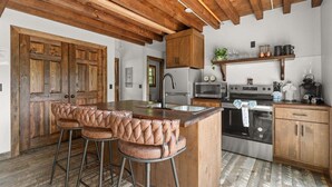 A kitchen with wooden cabinets, a stainless steel refrigerator, a microwave, an oven, and a bar area with leather stools. - Cozy Cabin Tucked Away w Free Attraction Tickets_Deck Space_Bonus Loft_Near Branson (Branson)