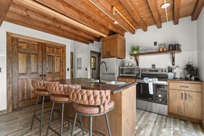 A kitchen with wooden cabinets, a stainless steel refrigerator, a microwave, an oven, and a bar area with leather stools. - Cozy Cabin Tucked Away w Free Attraction Tickets_Deck Space_Bonus Loft_Near Branson (Branson)