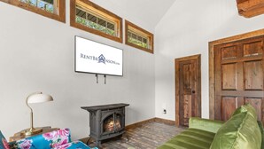A living room with a fireplace, a sofa, a television mounted on the wall, and a wooden door. - Cozy Cabin Tucked Away w Free Attraction Tickets_Deck Space_Bonus Loft_Near Branson (Branson)
