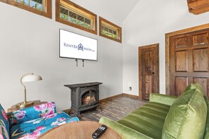 A living room with a fireplace, a television mounted on the wall, and a green sofa. - Cozy Cabin Tucked Away w Free Attraction Tickets_Deck Space_Bonus Loft_Near Branson (Branson)