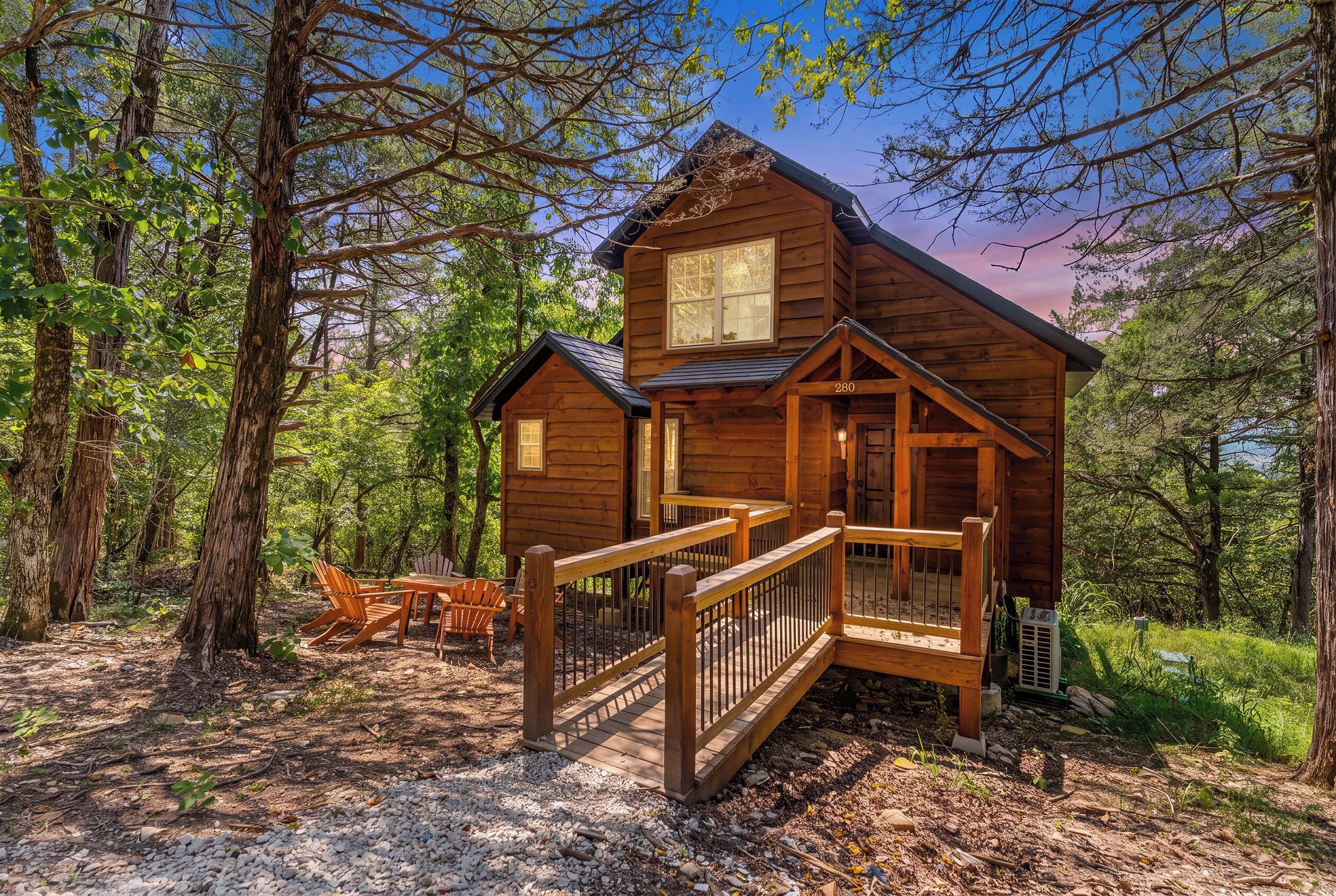 A wooden cabin with a porch and a deck, surrounded by trees.