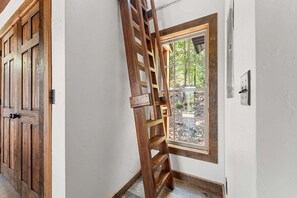 A wooden door with a metal handle, a window with a view of trees, and a wall-mounted light switch. - Tucked Away Cabin w Peaceful Views_Near Branson_Free Attraction Tickets (Branson)