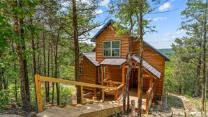 Eine Holzhütte mit Veranda und einer Holztreppe, die zu ihr hinaufführt, umgeben von Bäumen.