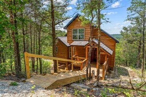 A wooden cabin with a porch and a wooden staircase leading up to it, surrounded by trees. - Tucked Away Cabin w Peaceful Views_Near Branson_Free Attraction Tickets (Branson)