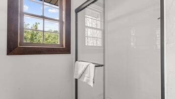 A bathroom with a glass shower door, a towel hanging on a rack, and a window with a wooden frame.