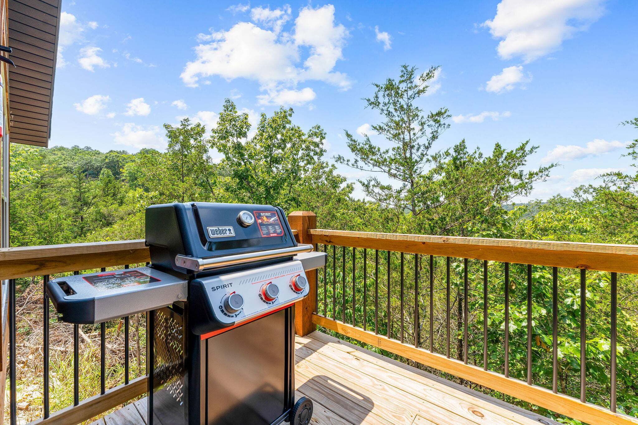 A Weber Spirit grill on an outdoor deck with a view of a forested area.