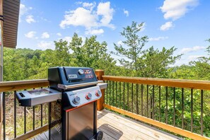 Ein Weber Spirit Grill auf einer Terrassenfläche mit Blick auf ein bewaldetes Gebiet.