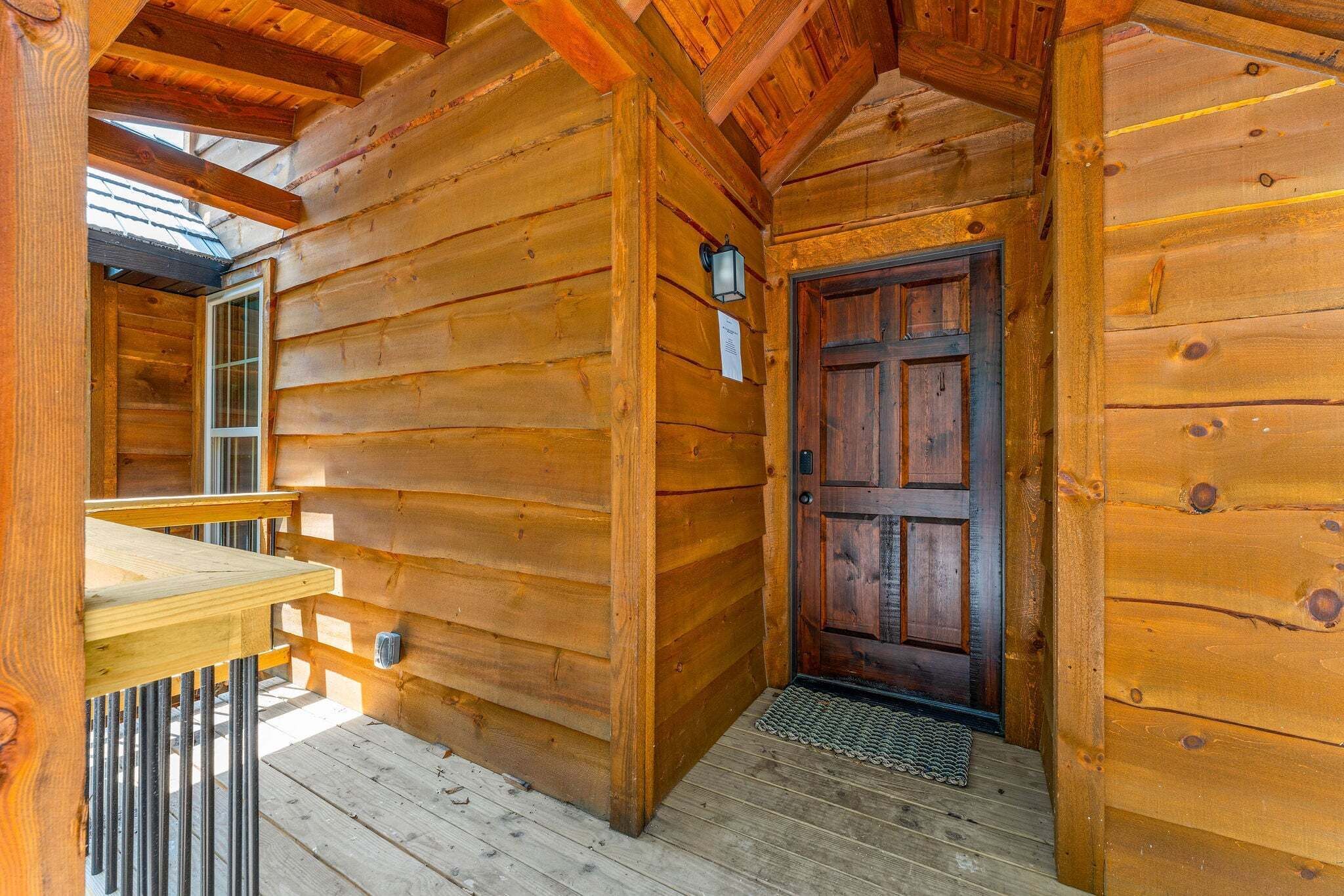 A wooden cabin interior with a wooden door, a small porch, and a window.