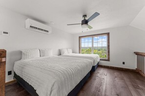 Ein Schlafzimmer mit einem großen Bett, einem Deckenventilator, einer Klimaanlage und einem Fenster mit Blick auf Grünflächen.