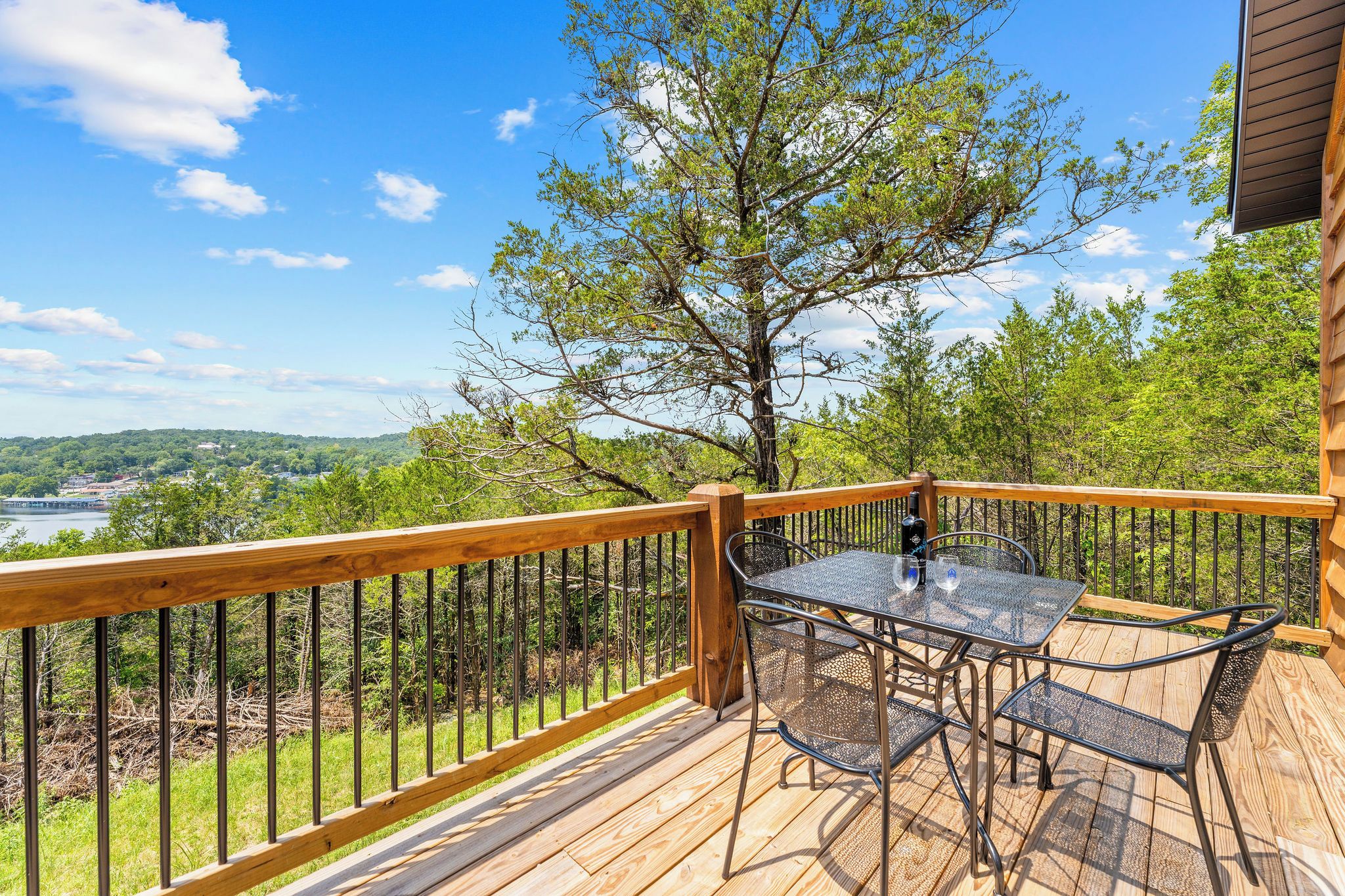 A wooden deck with a table and chairs, overlooking a scenic landscape with trees and a body of water.