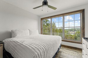 A bedroom with a large window, a bed with white bedding, and a ceiling fan. - Secluded Cabin_Lake Taneycomo View_Peaceful Deck_Bonus Loft_Free Attraction Tickets (Branson)