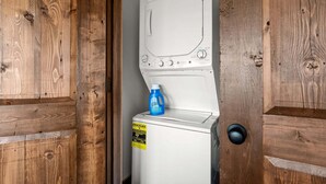 Una màquina de rentar blanca amb una ampolla de detergent blau a sobre, col·locada a un moble de fusta.