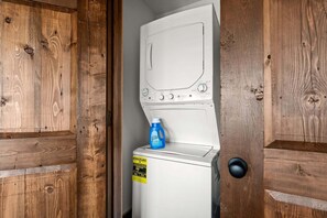 Eine weiße Waschmaschine mit einem blauen Waschmittelbehälter darauf, in einem Holzschrank platziert.