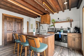 A kitchen with a wooden island, bar stools, a microwave, a stove, and wooden cabinets. - Secluded Cabin_Lake Taneycomo View_Peaceful Deck_Bonus Loft_Free Attraction Tickets (Branson)