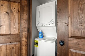 Eine weiße Waschmaschine mit einer blauen Flasche Waschmittel darauf, einem gelben Energieausweis und einem schwarzen Klingelknopf.