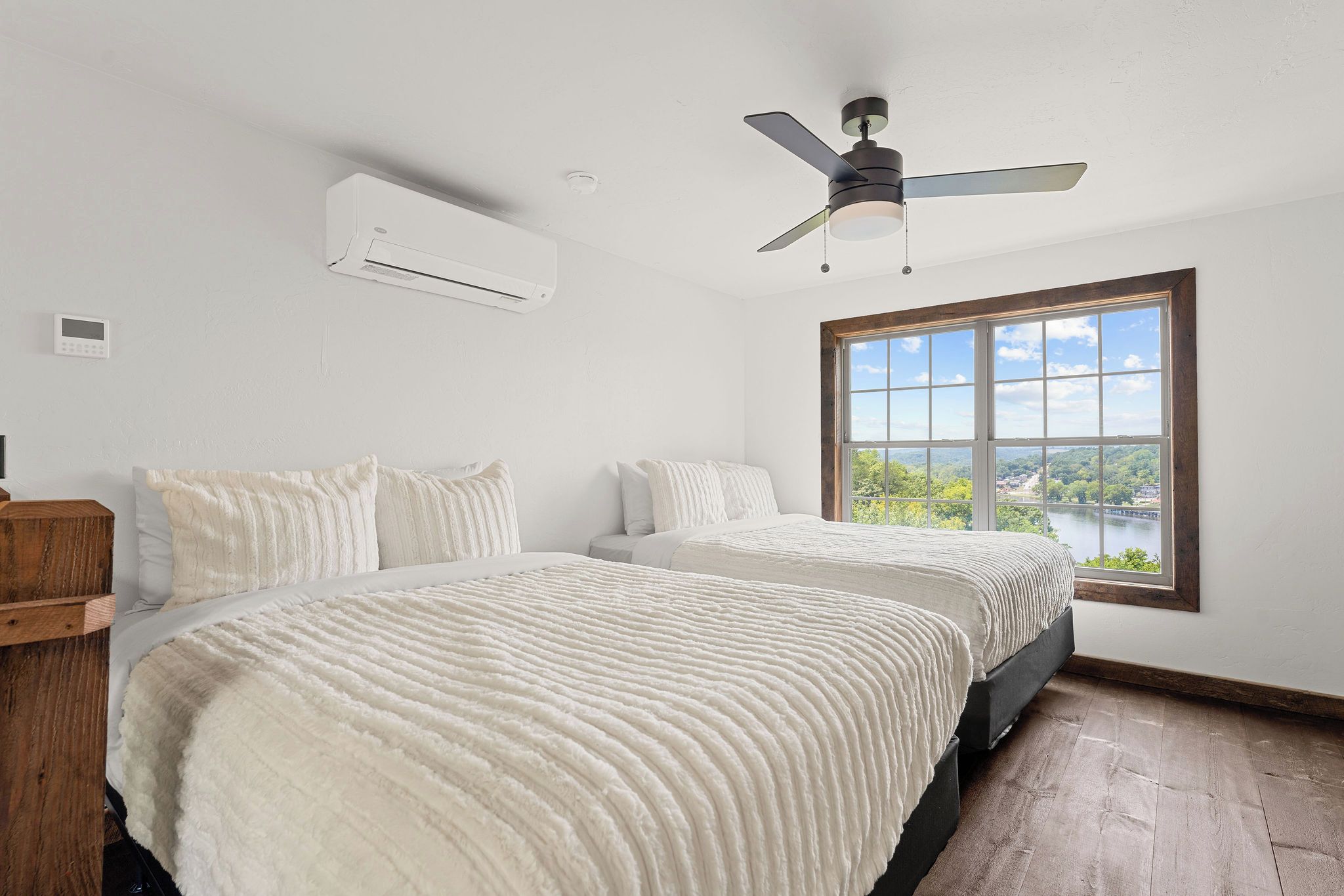 A bedroom with two beds, a ceiling fan, an air conditioning unit, and a large window with a view.