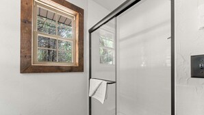 Un bany amb una cabina de dutxa de vidre, una finestra amb marc de fusta i un suport per a tovalloles.