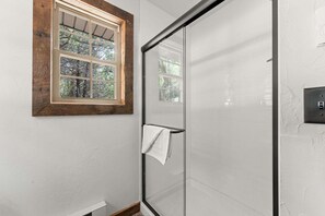 A bathroom with a glass shower enclosure, a wooden-framed window, and a towel rack.