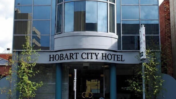 Un bâtiment moderne doté d’une façade en verre incurvée, d’une entrée imposante et d’une enseigne indiquant « HOBART CITY HOTEL ».