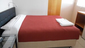 Une chambre d’hôtel avec un lit, une table de chevet, une lampe et une petite table en bois.
