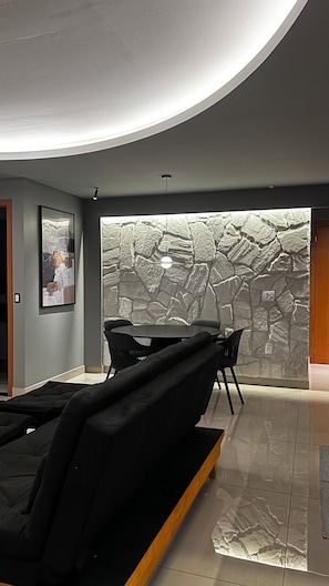 A modern interior with a stone wall, black sofas, and a framed picture on the wall. - Fully furnished apartment | Excellent location with garage (Goiânia)
