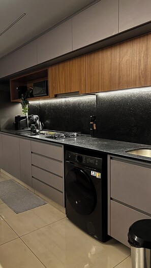 A modern kitchen with a built-in washing machine, a microwave, and a coffee maker. - Fully furnished apartment | Excellent location with garage (Goiânia)