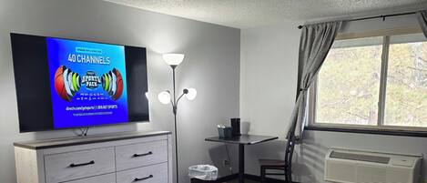 A hotel room with a bed, a desk, a chair, a television, a lamp, and a window.