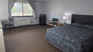 Hotellihuone, jossa on sänky, työpöytä, tuoli, televisio, lamppu ja ikkuna, jossa on verhot.