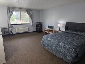 A hotel room with a bed, a desk, a chair, a TV, a lamp, and a window with curtains.